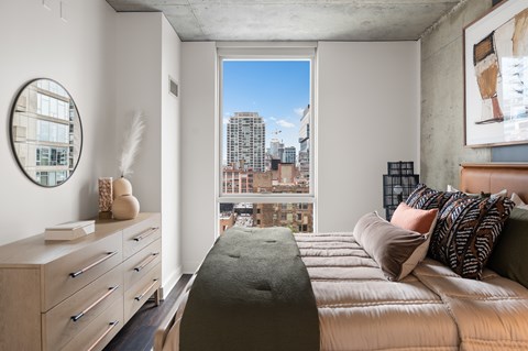 A bedroom with a large bed and a city view through the window.