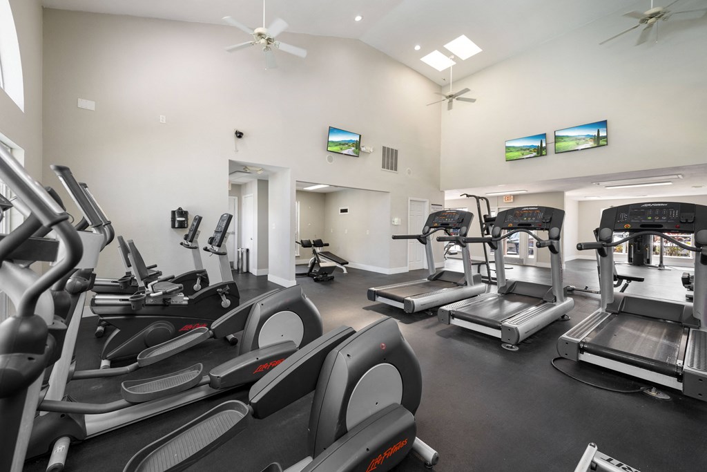 a gym with cardio equipment and flat screen tvs