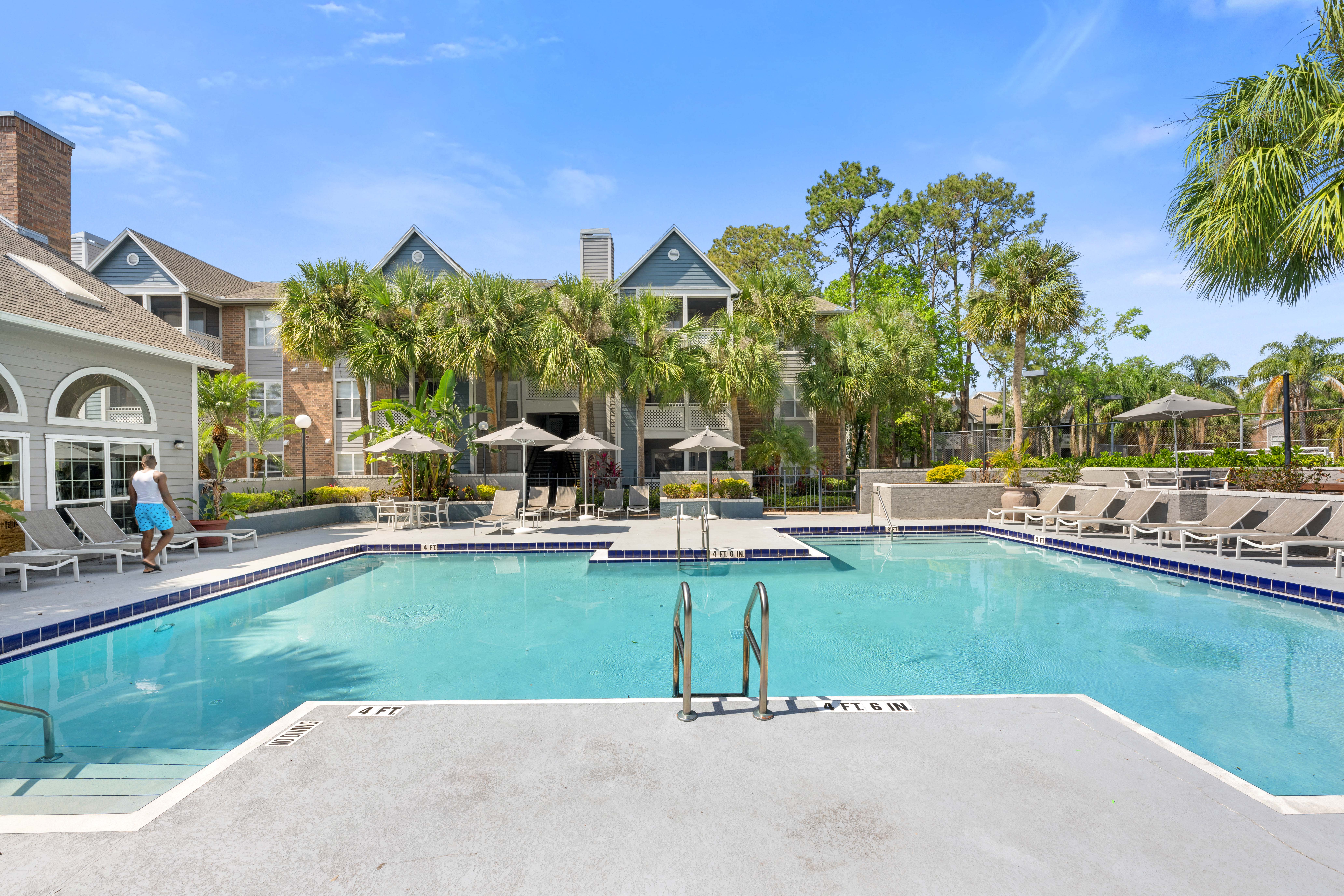 a large swimming pool with lounge chairs and umbrellas in front of a building