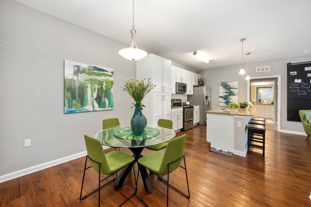 a dining area with a glass table and chairs and a kitchen in the background