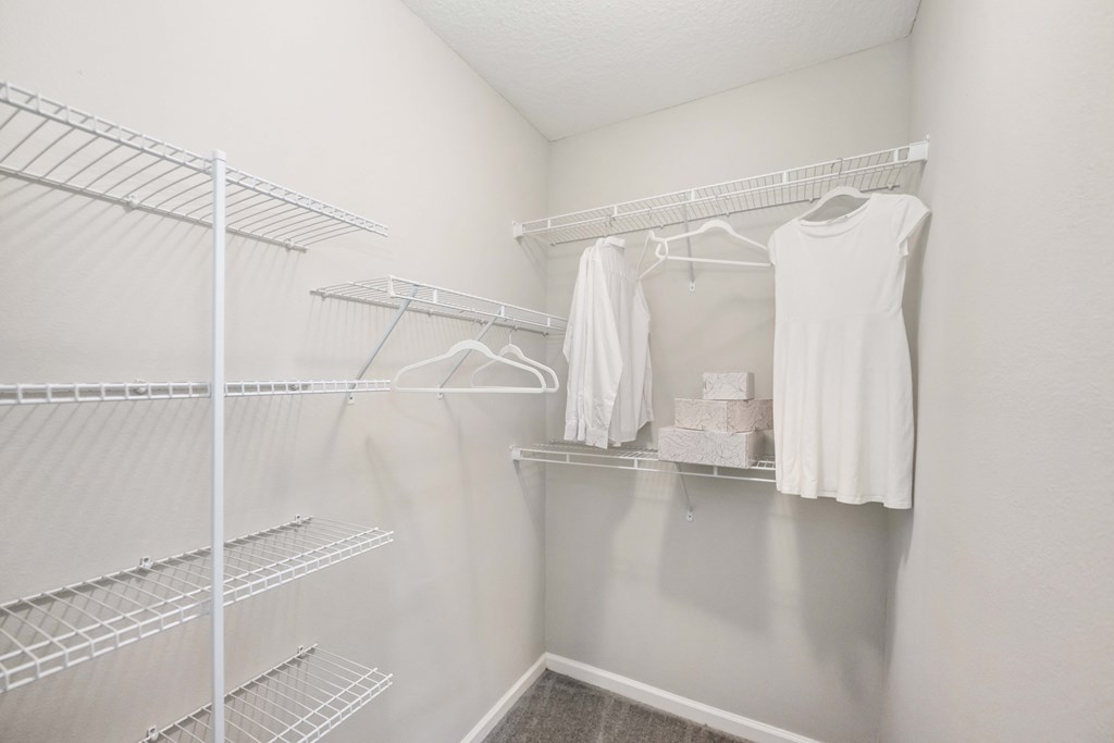 a walk in closet in a bedroom with white walls and a white dress hanging on the wall