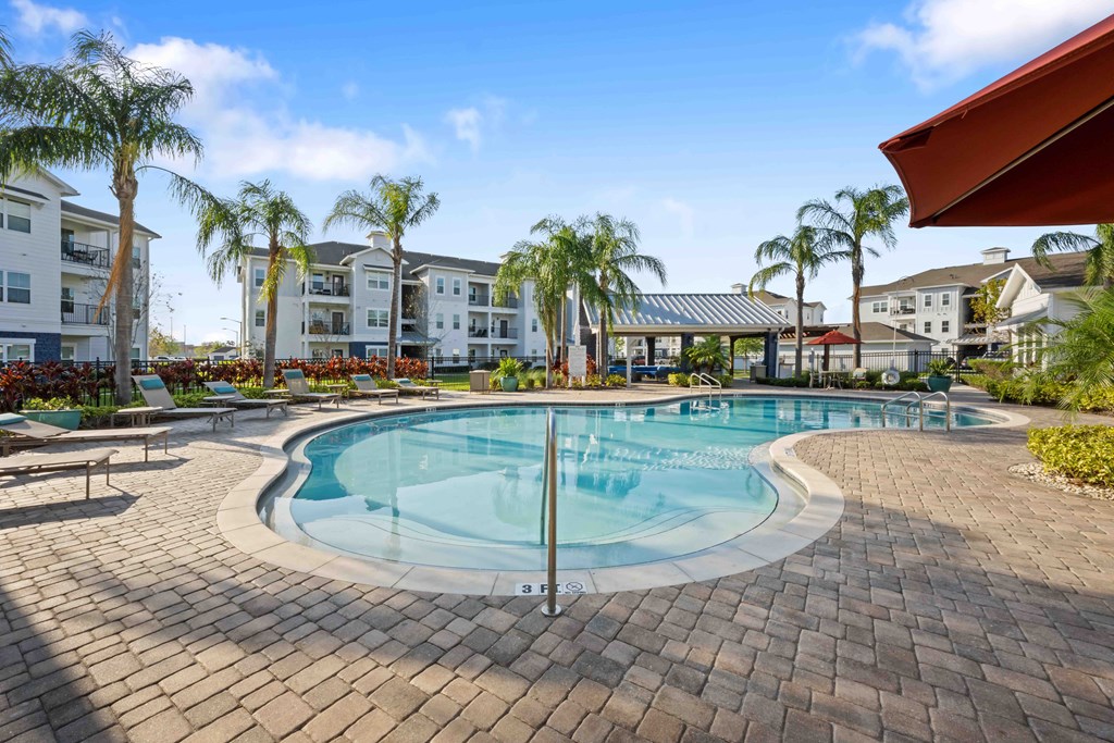 a resort style swimming pool with chaise lounge chairs and palm trees in the background