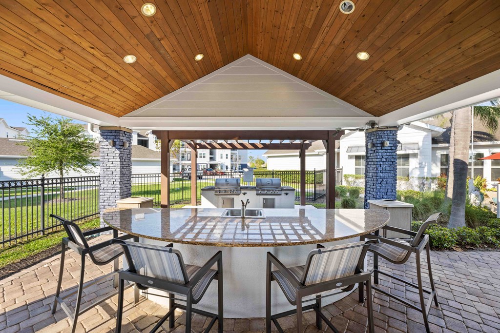 a patio with a large circular table and chairs with a grill in the background