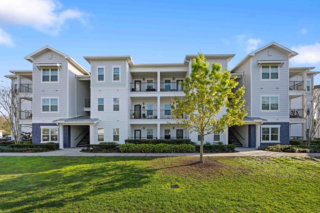 an apartment building with white siding and a tree in front of it