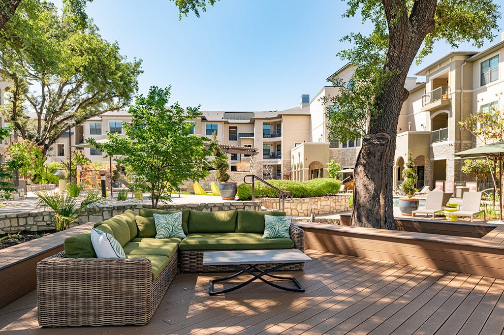 A patio with a green couch and a tree in front of apartment buildings.