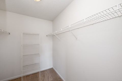a spacious closet with white walls and shelves and a mirrored closet rack on the wall