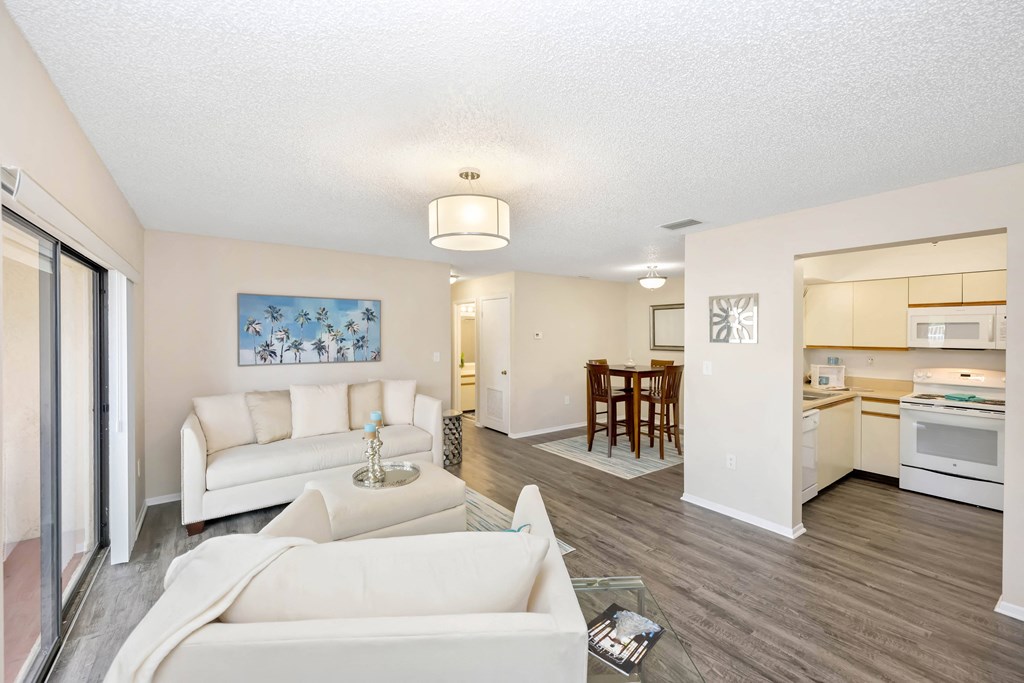 a living room with white couches and chairs and a kitchen in the background