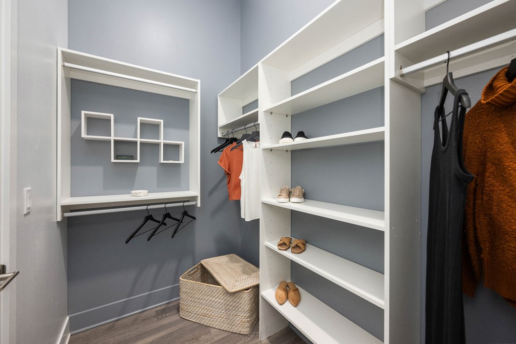 a walk in closet with white shelves and grey walls