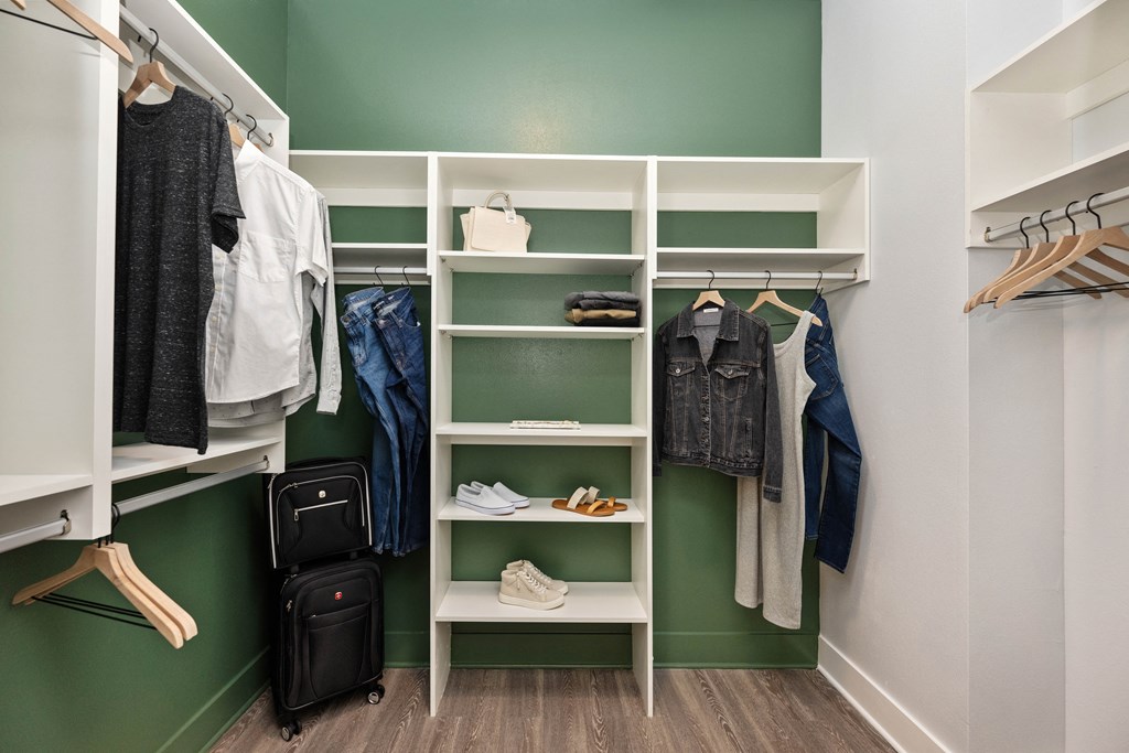 a walk in closet with white shelving and a green wall