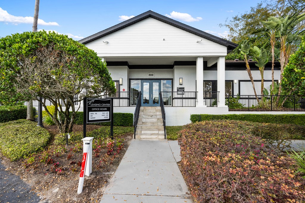 the front of a white building with a sidewalk and a black sign