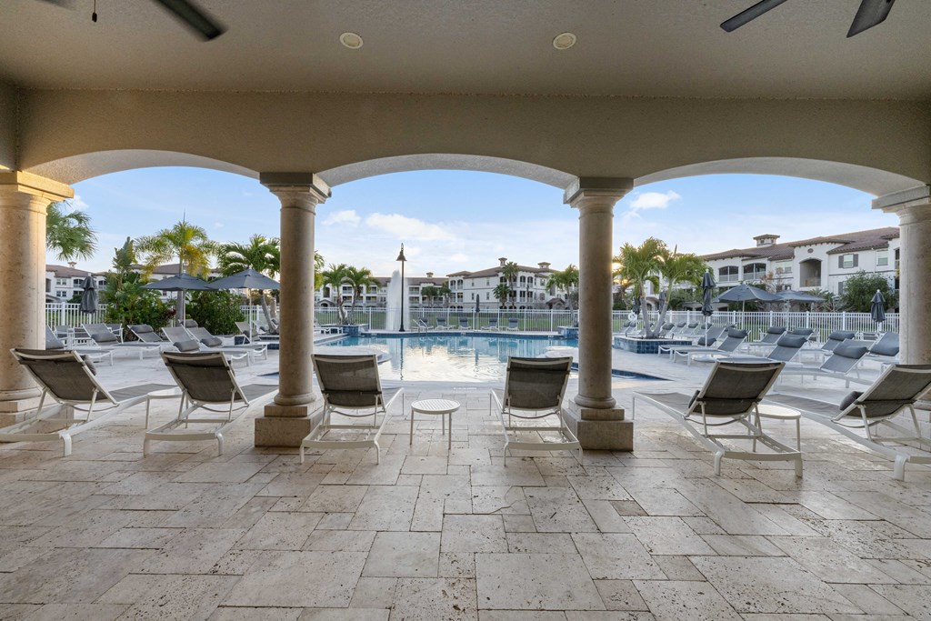 a view of a swimming pool with chairs and a patio with columns