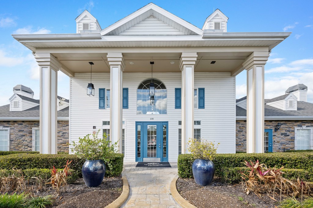 the front facade of a white house with blue doors and columns