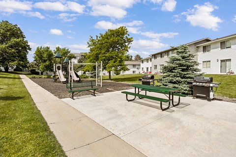 A playground with a slide, swings, and a picnic table in a park.