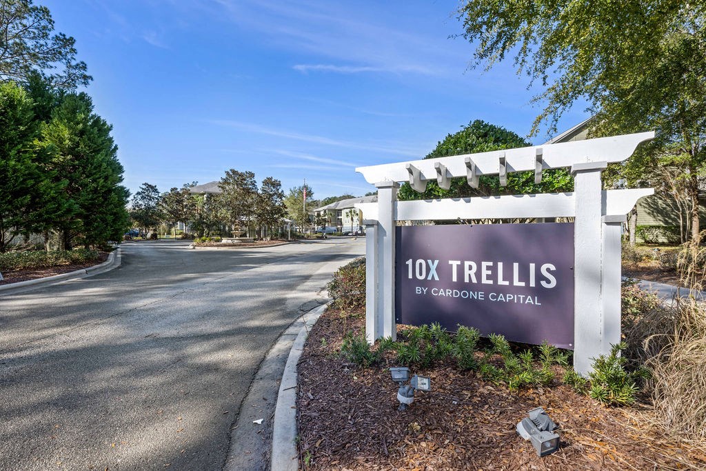 A sign for 10X Trellis by Gardone Capital stands in front of a tree-lined street.