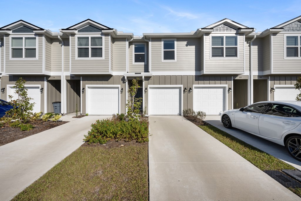A white car is parked in front of a grey house.