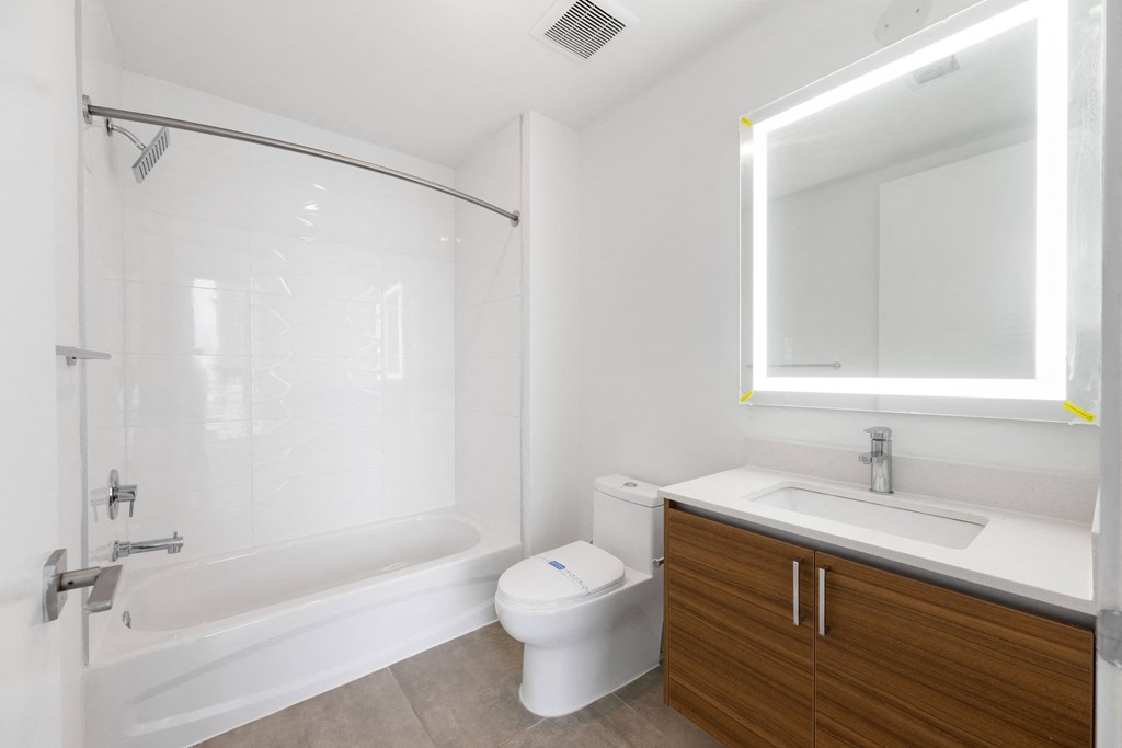 a bathroom with a white toilet next to a white bathtub and a wooden vanity with a