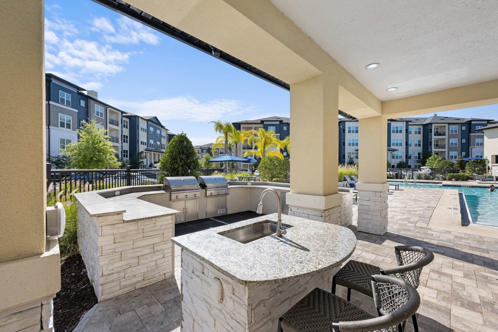 an outdoor kitchen with a bar and a grill next to a swimming pool
