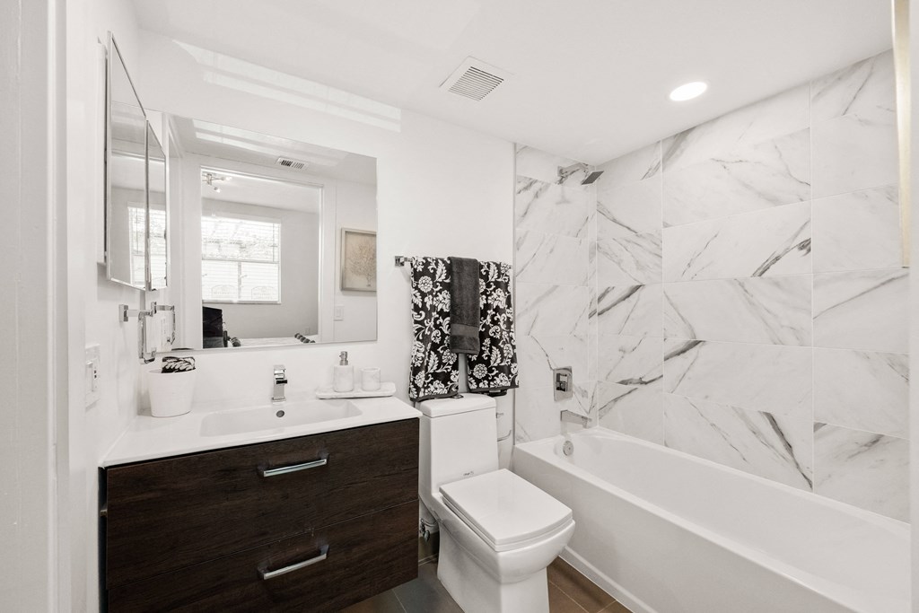 a bathroom with white and black marble walls and a white tub and shower and a