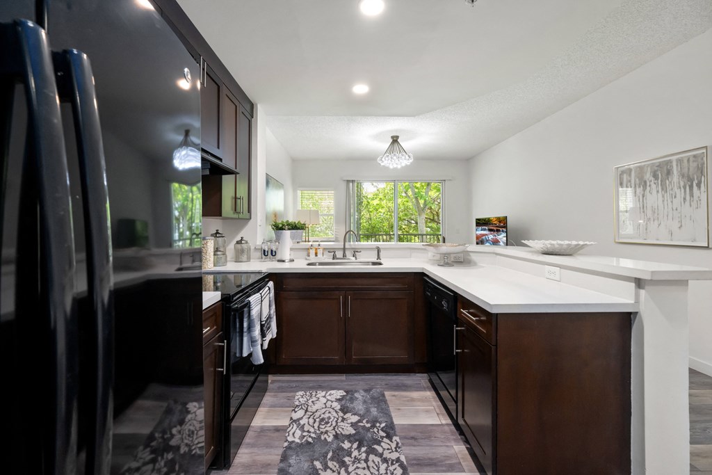 a kitchen with white countertops and dark cabinets and a black refrigerator