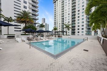 a large swimming pool with chaise lounge chairs and umbrellas in front of a tall