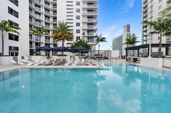 a large swimming pool with chaise lounge chairs and umbrellas in front of a large