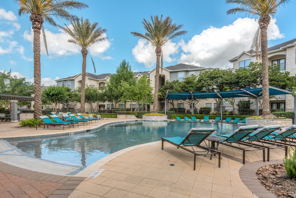 A pool surrounded by palm trees and lounge chairs.