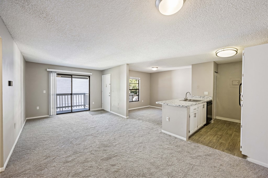 an empty living room and kitchen with a door to a balcony