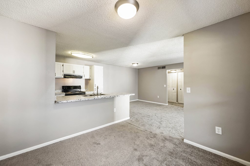an empty living room and kitchen with a granite counter top