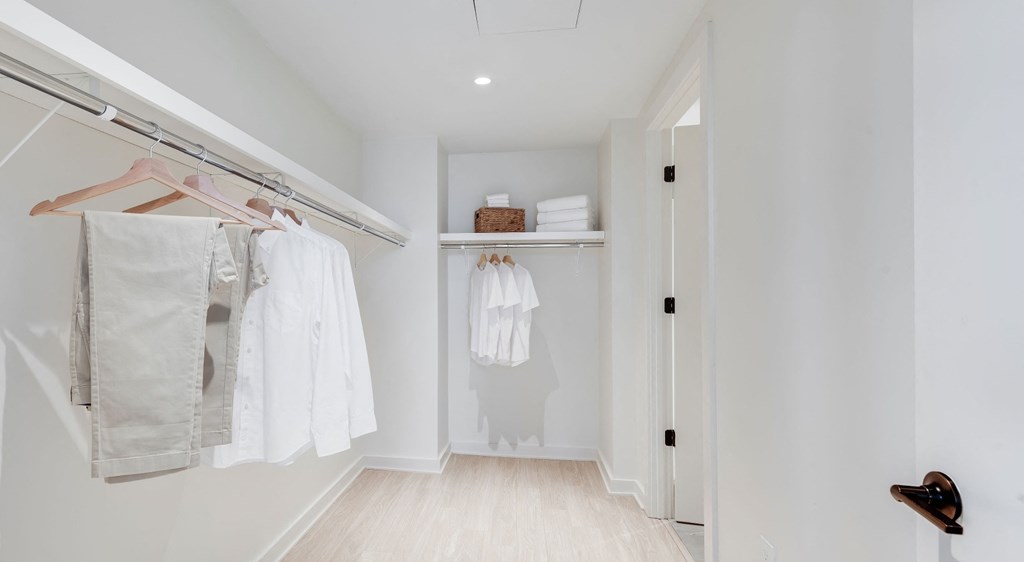 A white closet with clothes hanging and a door on the right.
