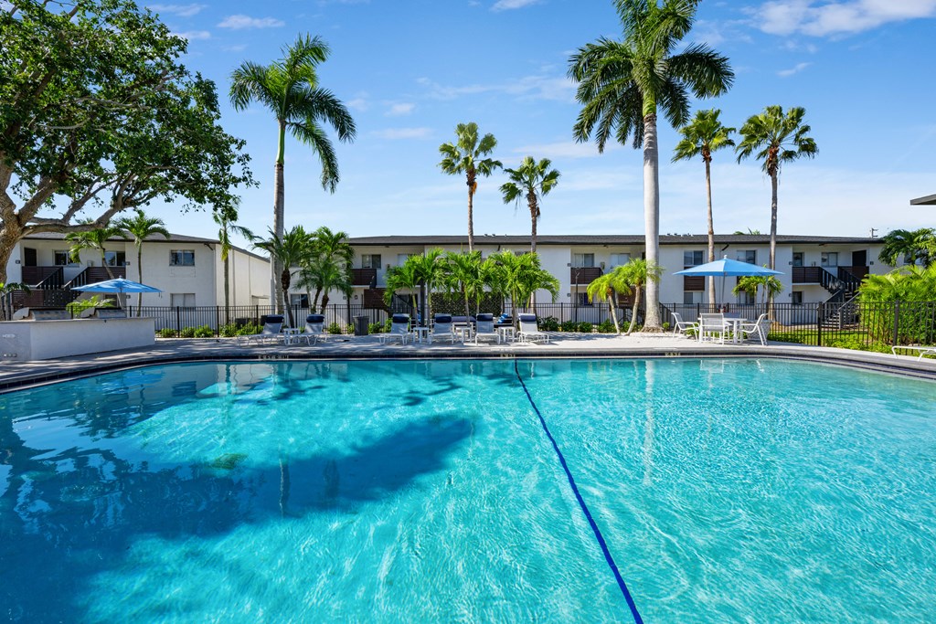 a large swimming pool with palm trees and a building in the background