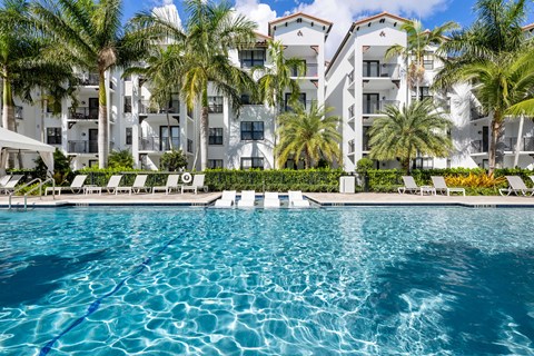 A swimming pool in front of a white building with palm trees.