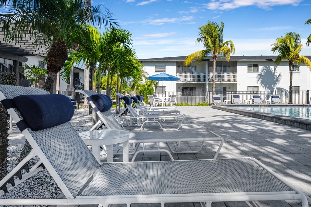 a pool with chairs and tables and a building in the background
