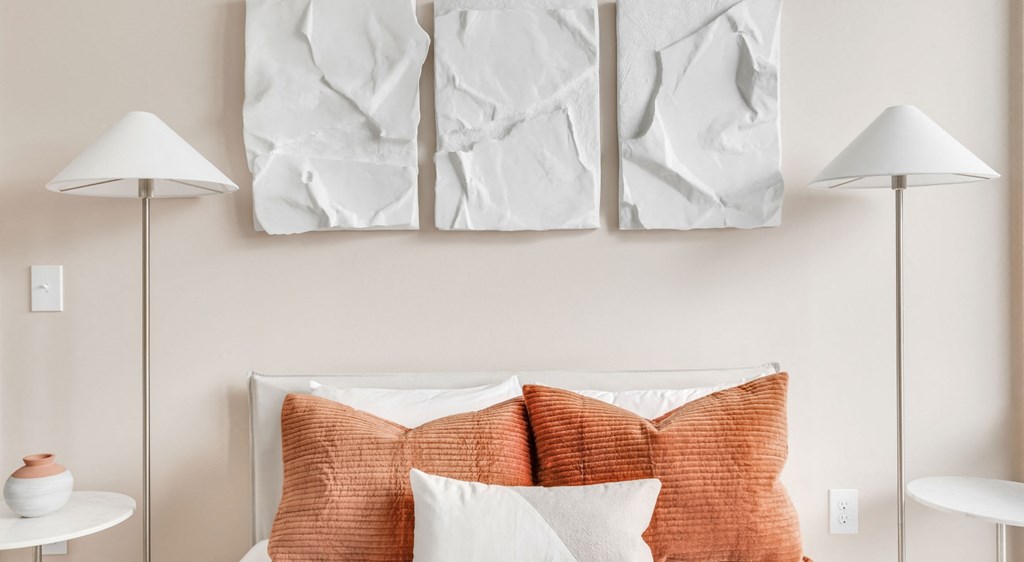 A bed with orange pillows and white bedding sits under a painting.