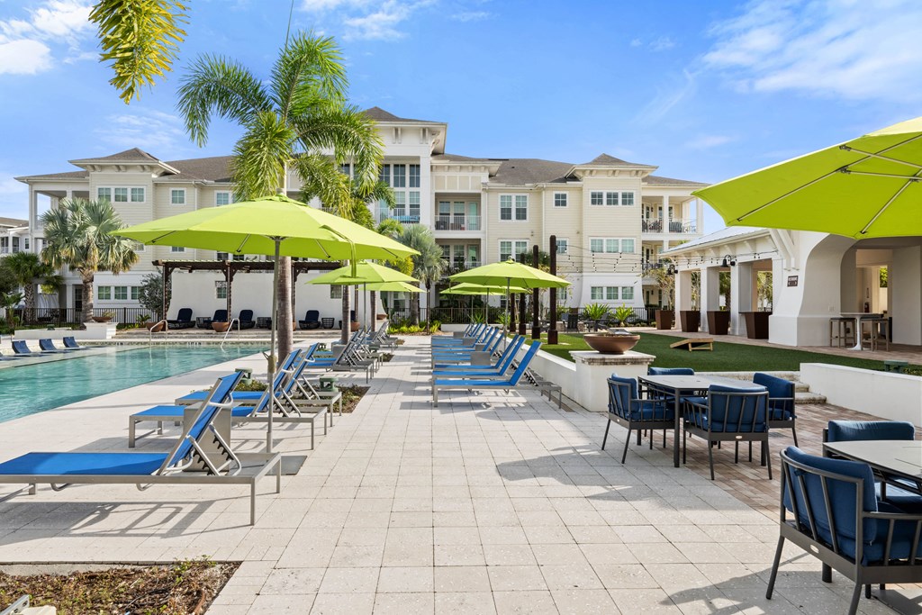 a pool with blue chairs and yellow umbrellas and buildings in the background
