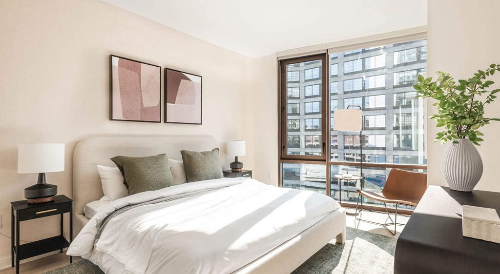 A bedroom with a large bed and a view of a cityscape through the window.