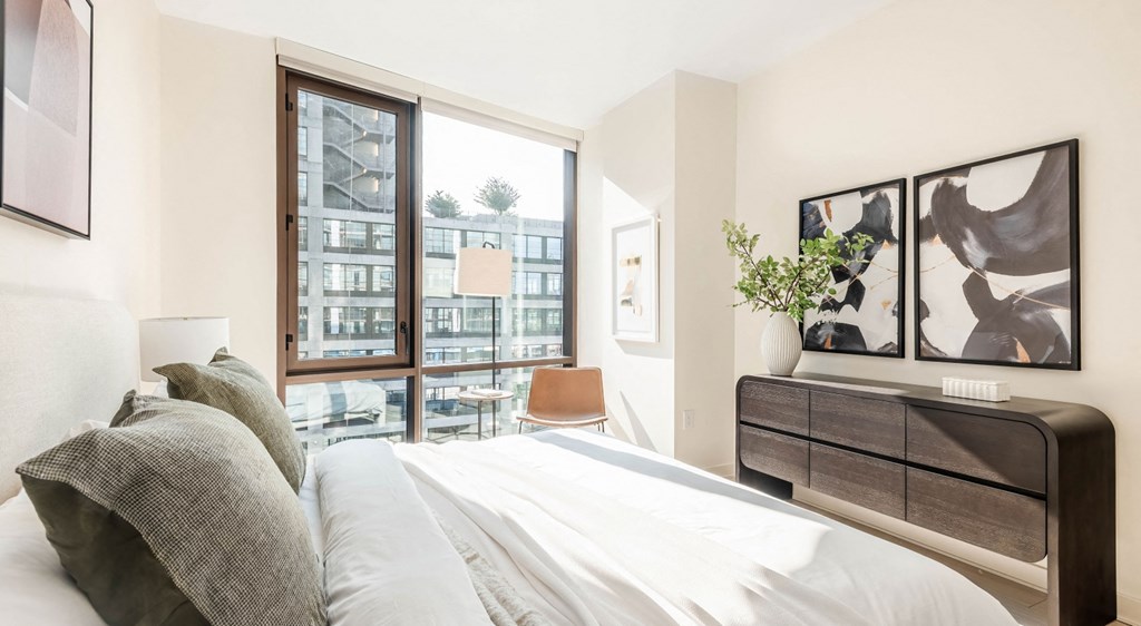 A bedroom with a large bed and a view of a cityscape through the window.