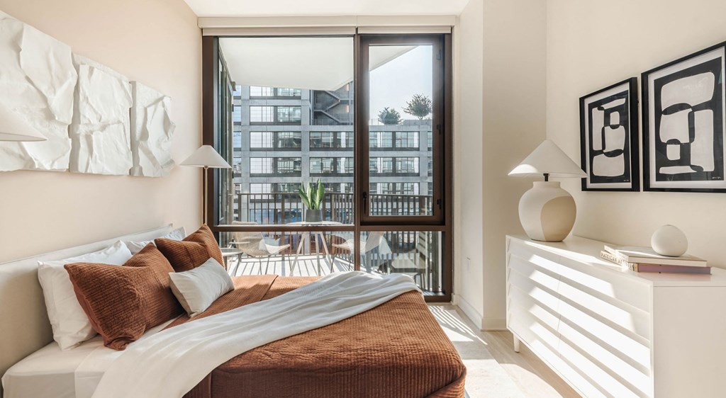 A bedroom with a large bed and a view of a cityscape through the window.