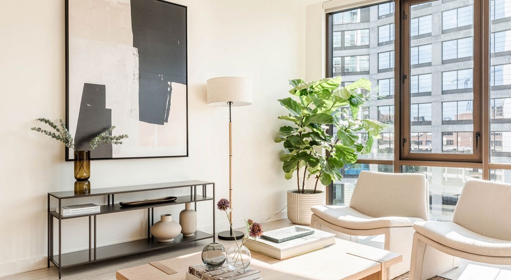 A living room with a large painting on the wall, a white sofa, a coffee table with books and vases, and a potted plant.