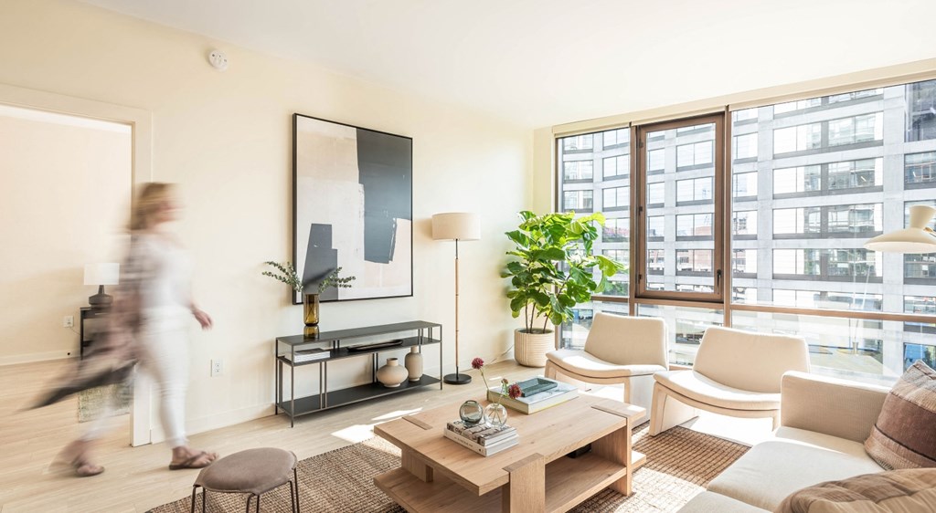A woman walks through a living room with a large window.