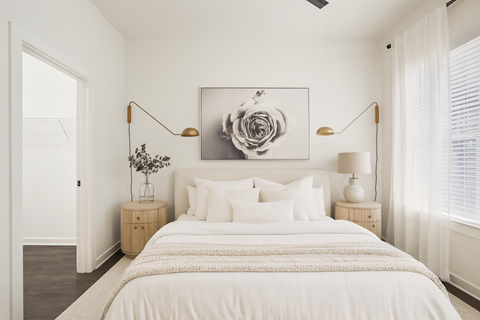 A bedroom with a large bed, a painting above it, and two lamps on either side of the bed.