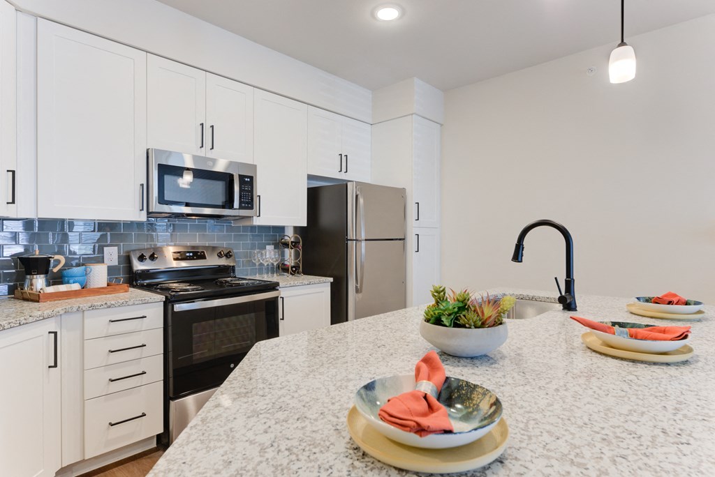 a kitchen with white cabinets and black appliances and a marble counter top