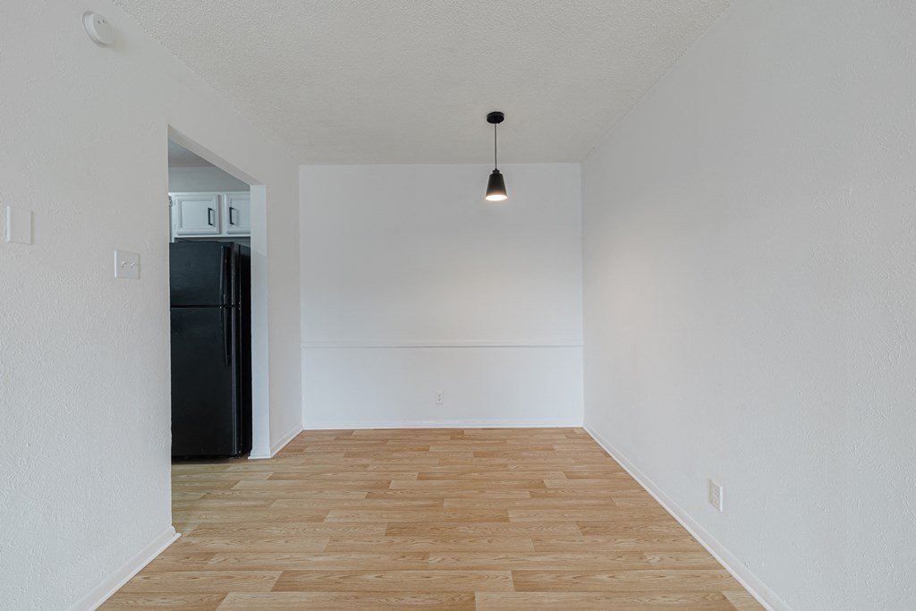 an empty living room with wood flooring and a black refrigerator