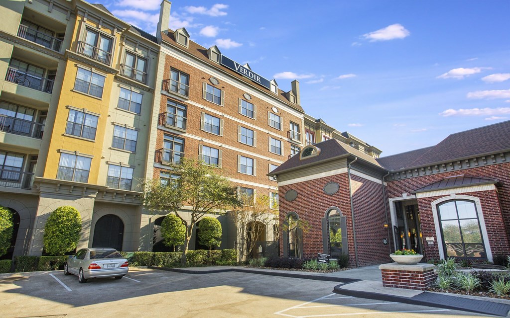 A car is parked in a sunny lot in front of a building with a brick entrance.