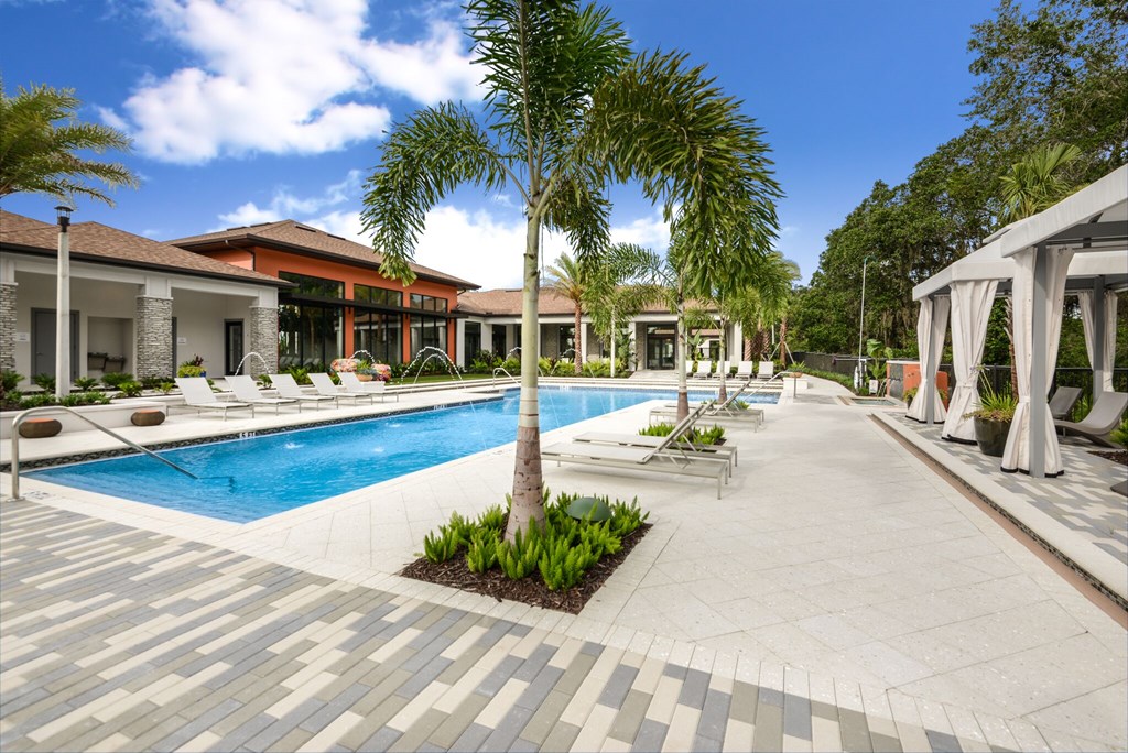 A pool surrounded by a tiled walkway and palm trees.