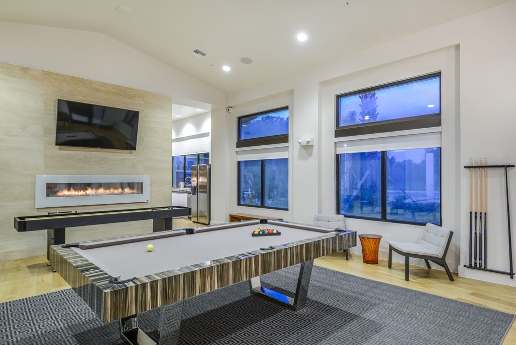 A billiard table is in the middle of a room with a fireplace and a television.