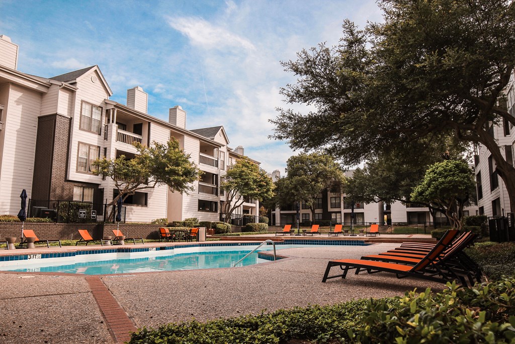 a swimming pool with orange chairs in front of an apartment building