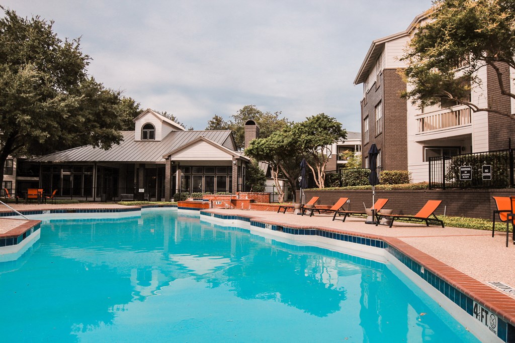 a swimming pool with orange chairs and a building in the background