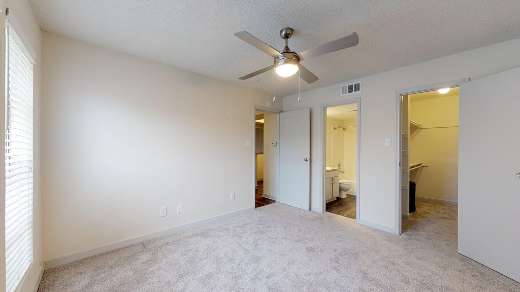 an empty living room with a ceiling fan and a door to a bathroom