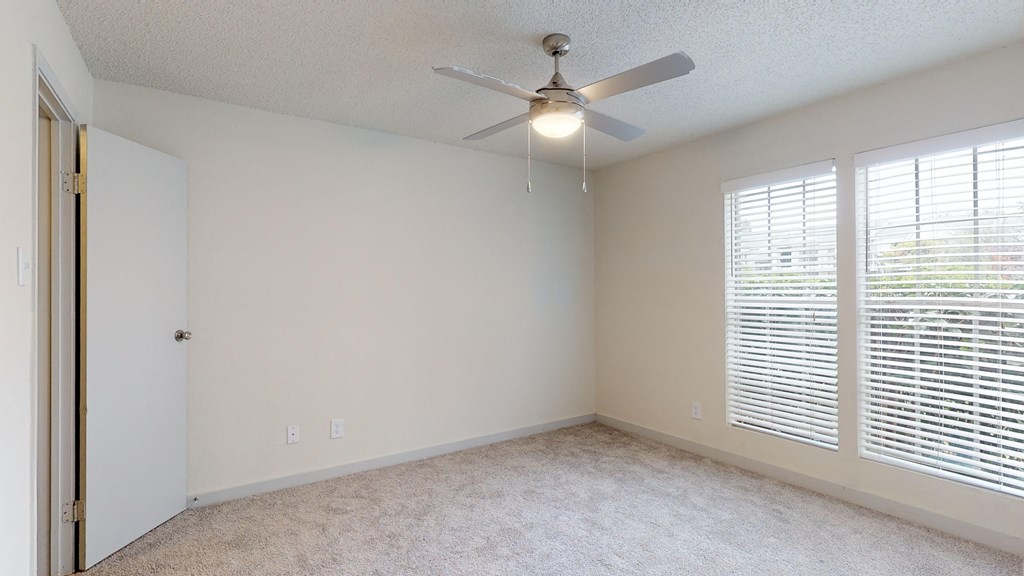 an empty bedroom with a ceiling fan and large windows