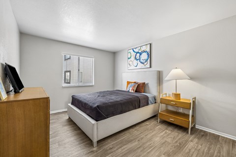 A bedroom with a bed, nightstand, and a painting on the wall.